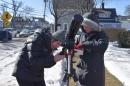 Two female students dressed in warm winter gear try to set up a telescope outside near a snow-covered sidewalk.